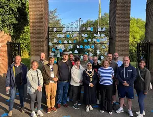The Mayor of Solihull with employees from Veolia, Solihull Council and members of Men's Walking and Talking group standing in front of Malvern Gates. The gates are covered with blue hearts which have positive messages written on them for people struggling with mental health